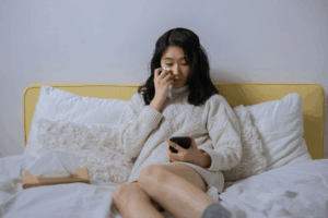 Femme asiatique cheveux noirs sur son lit devant son téléphone.