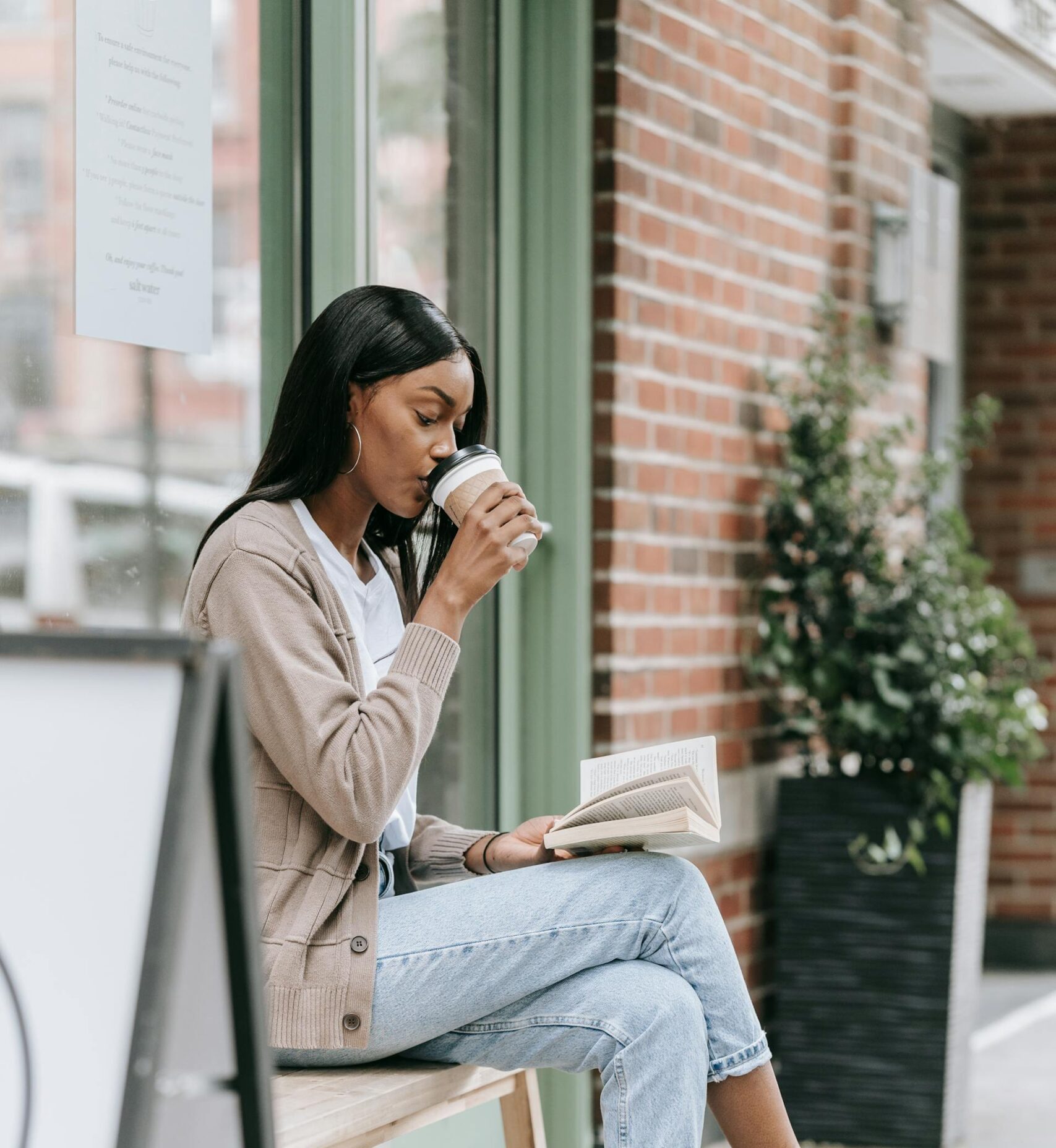 Femme noire en train de lire un livre dehors en buvant du café