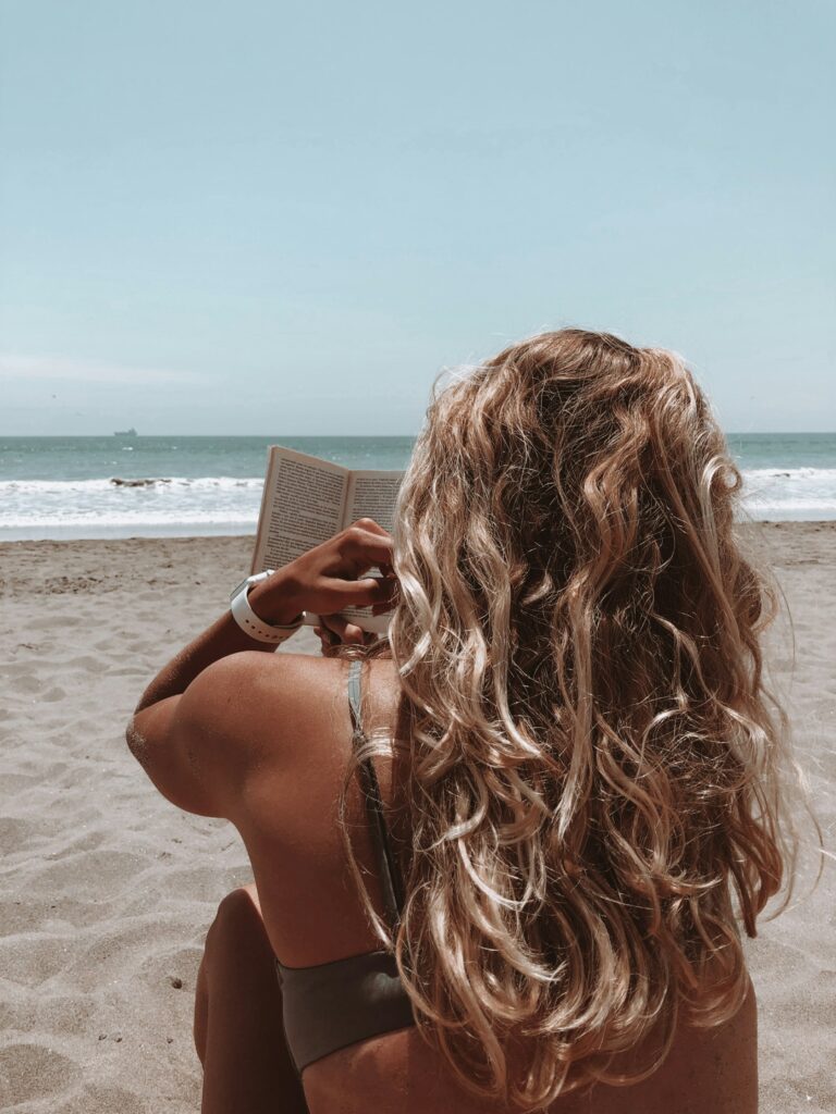 Femme blanche blonde lisant un livre à la plage