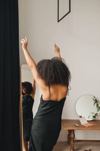 femme métisse qui se regarde dans le miroir avec une robe noire
