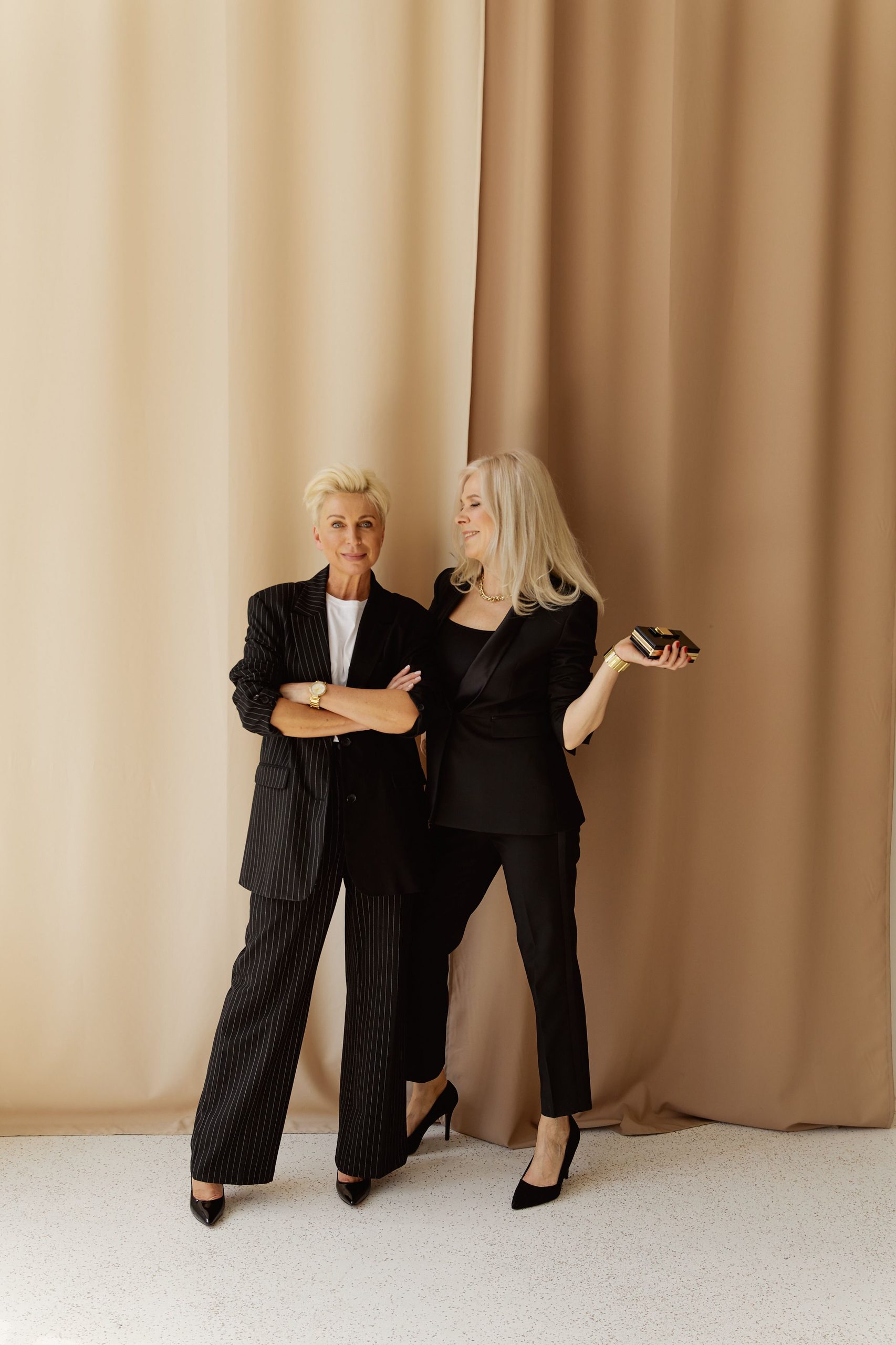 Deux femmes blanches et blondes d'une cinquantaineportant des tailleurs et blazers noirs