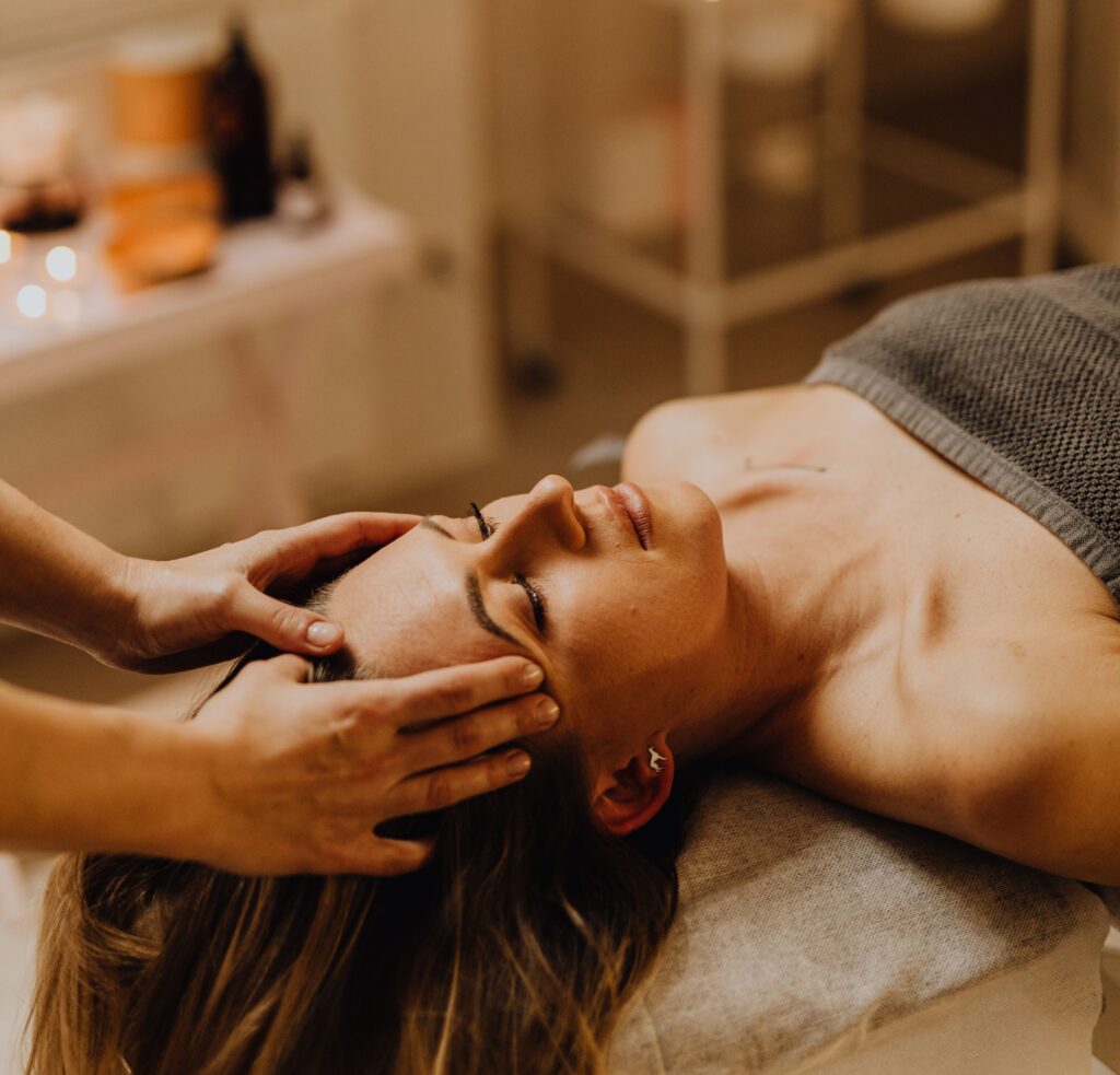 Une femme recevant un massage facial apaisant dans un environnement de spa serein avec un éclairage chaud.