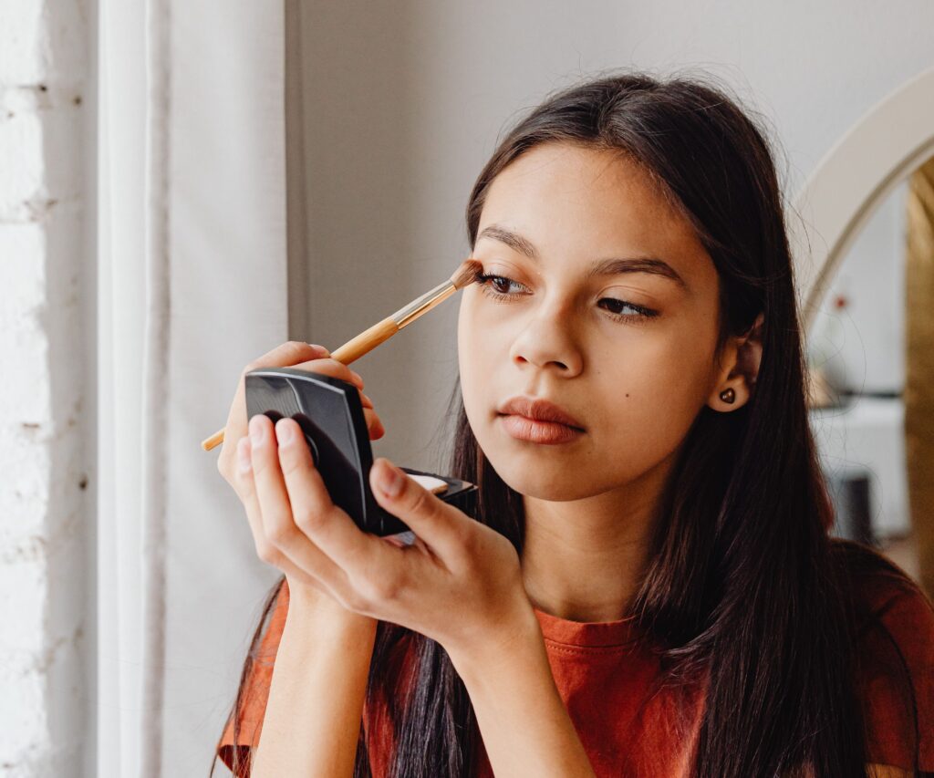 Jeune femme appliquant du maquillage pour les yeux avec un miroir de poche dans un cadre intérieur confortable.