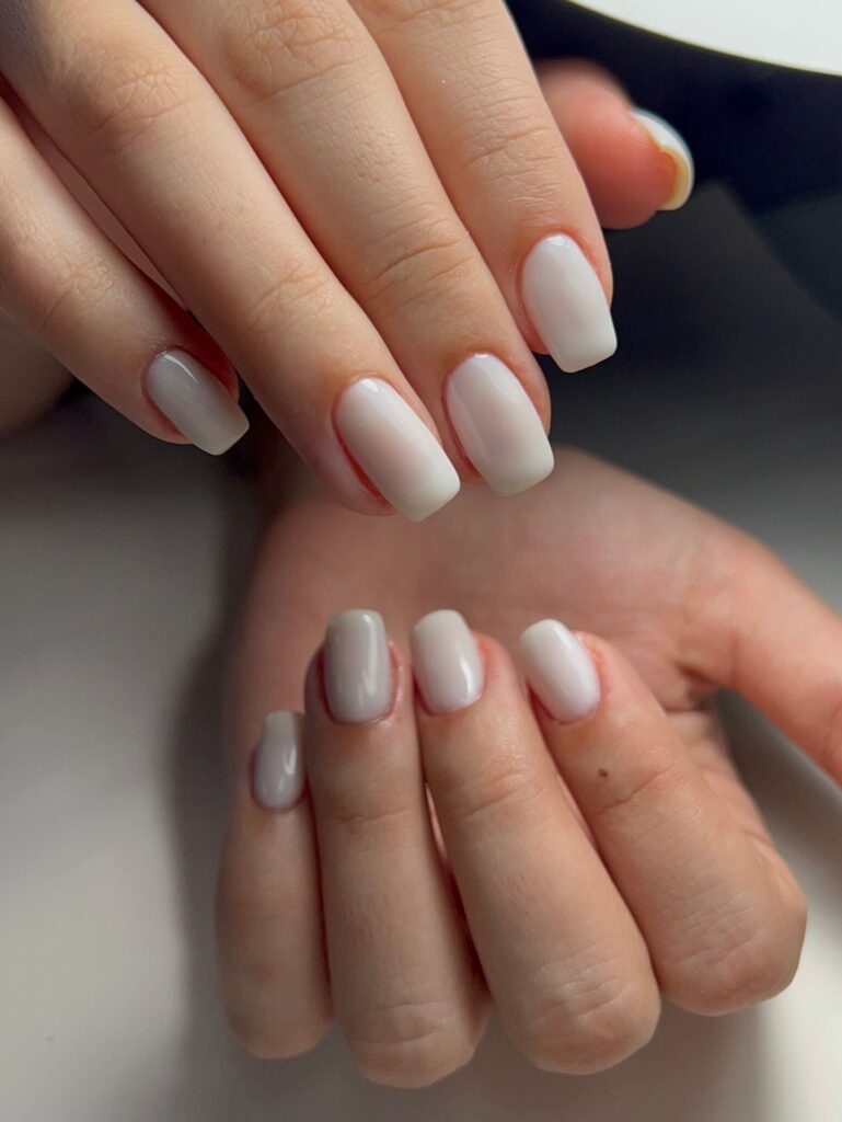 Gros plan élégant de mains avec du vernis à ongles rose pâle sous une lumière de lampe. 