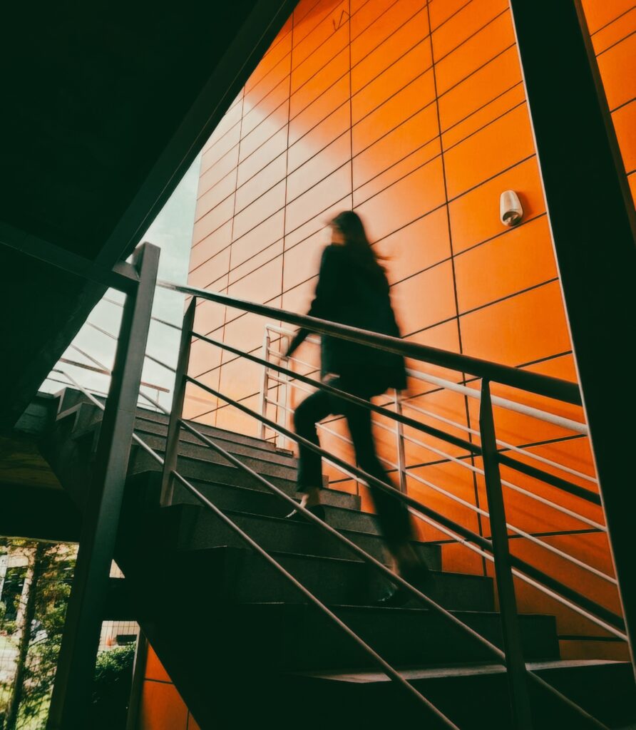 Une scène dynamique montrant une femme en mouvement dans un escalier contemporain aux murs d'un orange éclatant.